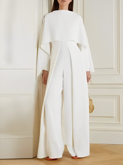 Tuta elegante bianca da donna con mantella, design moderno, indossata in interni. Perfetta per eventi formali e cerimonie.