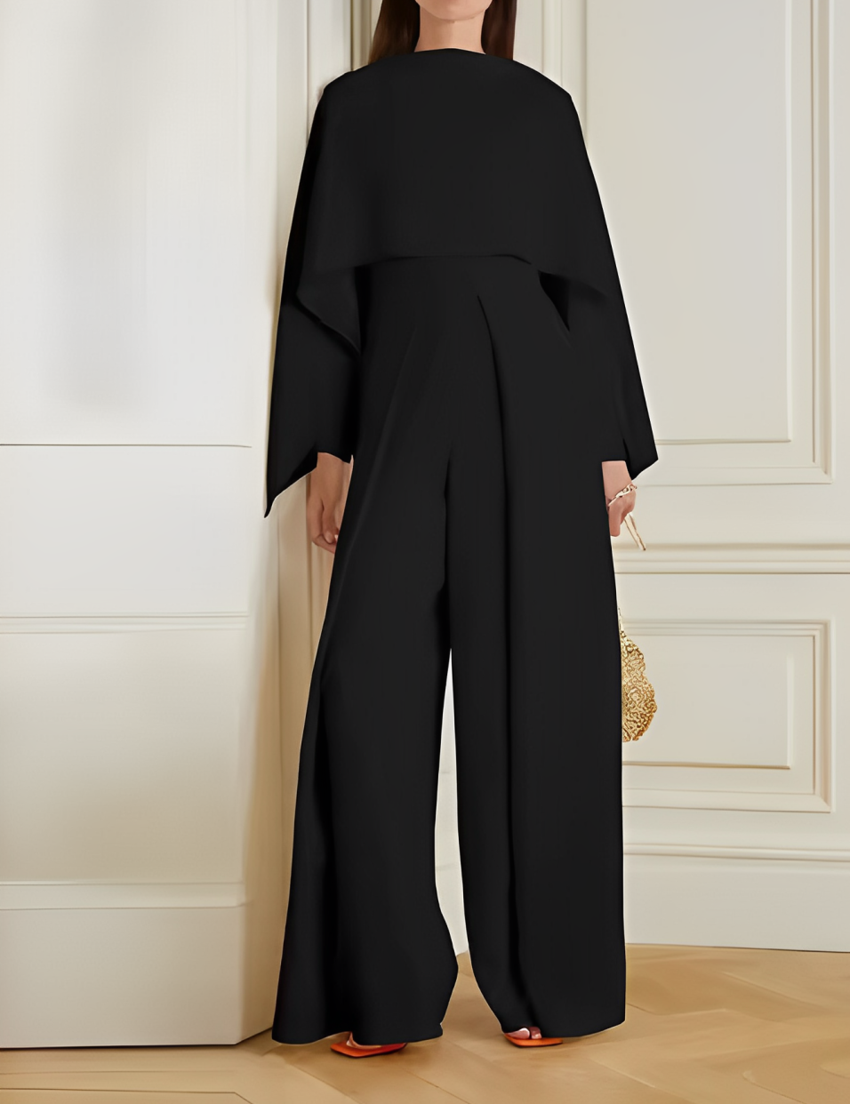 Tuta elegante nera da donna, design moderno con maniche ampie, indossata in un ambiente interno sofisticato. Accessorio borsa dorata.