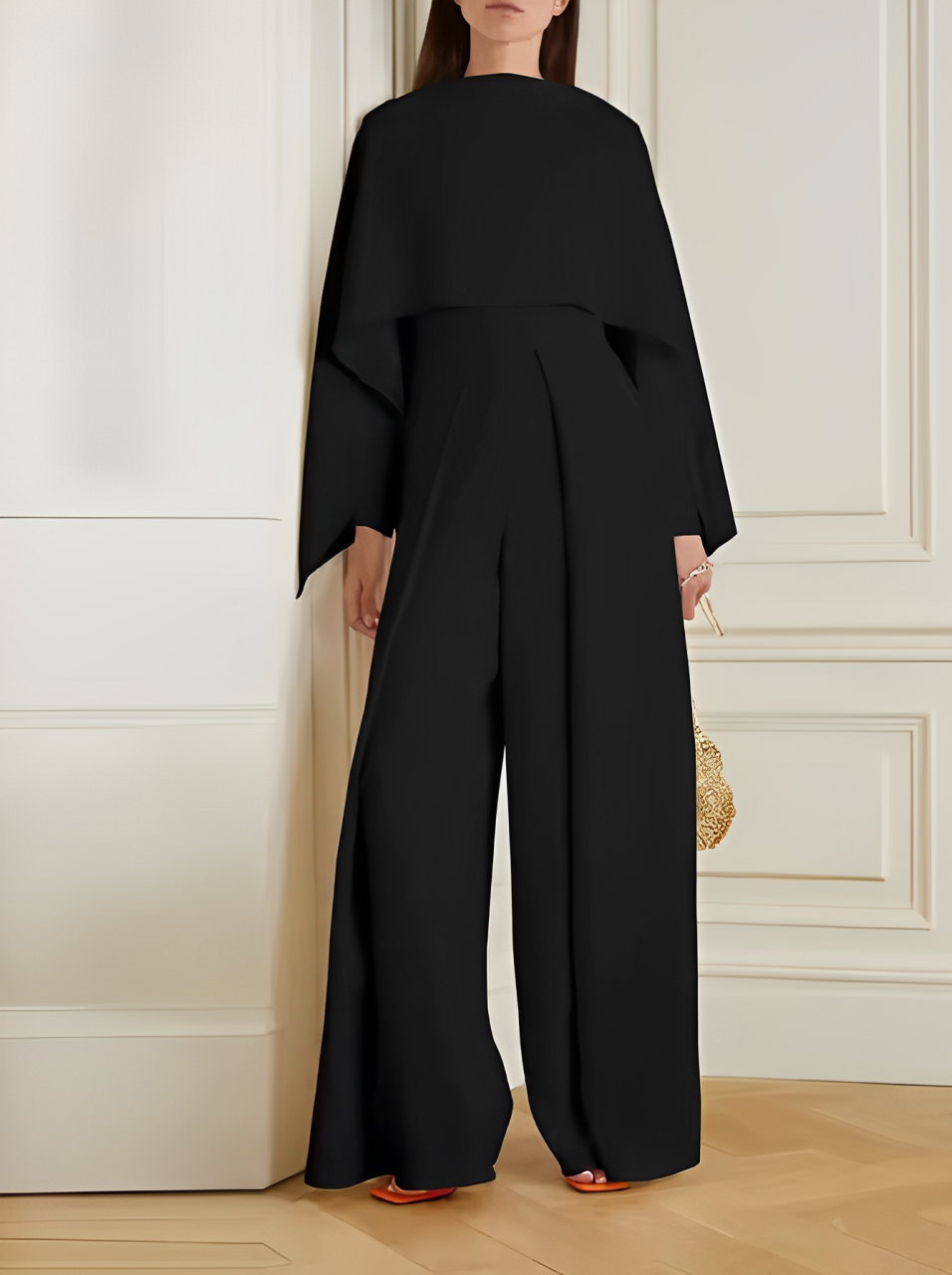 Tuta elegante nera da donna, design moderno con maniche ampie, indossata in un ambiente interno sofisticato. Accessorio borsa dorata.