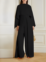 Tuta elegante nera da donna, design moderno con maniche ampie, indossata in un ambiente interno sofisticato. Accessorio borsa dorata.
