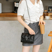 Donna con camicia bianca e gonna grigia, borsa a tracolla nera trapuntata, tiene bicchiere di caffè. Moda casual elegante, accessori femminili.