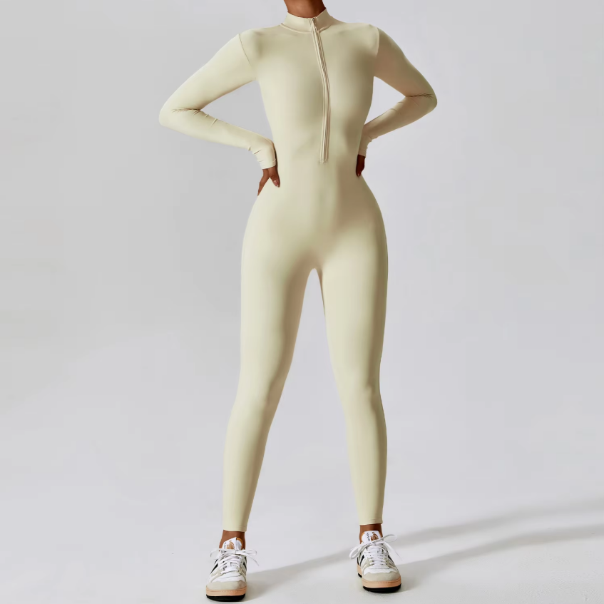 Tuta intera beige a maniche lunghe con zip frontale, indossata con sneakers bianche. Abbigliamento sportivo donna, moda fitness elegante.