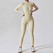 Tuta intera beige a maniche lunghe con zip frontale, indossata con sneakers bianche. Abbigliamento sportivo donna, moda fitness elegante.