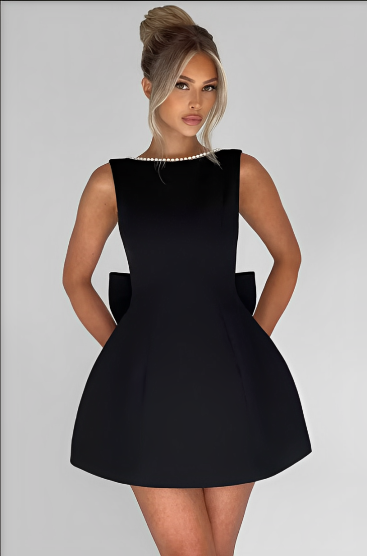 Donna in elegante abito nero senza maniche con collana di perle, sfondo bianco. Moda femminile, abbigliamento da sera, stile sofisticato.