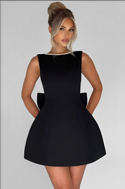 Donna in elegante abito nero senza maniche con collana di perle, sfondo bianco. Moda femminile, abbigliamento da sera, stile sofisticato.