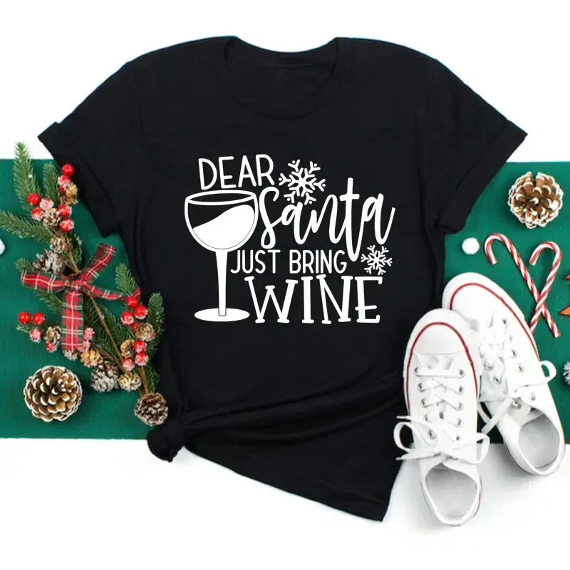 Maglietta nera con scritta "Dear Santa Just Bring Wine", decorata con bicchiere di vino, fiocchi di neve; accanto scarpe bianche, pigne e bastoncini di zucchero.