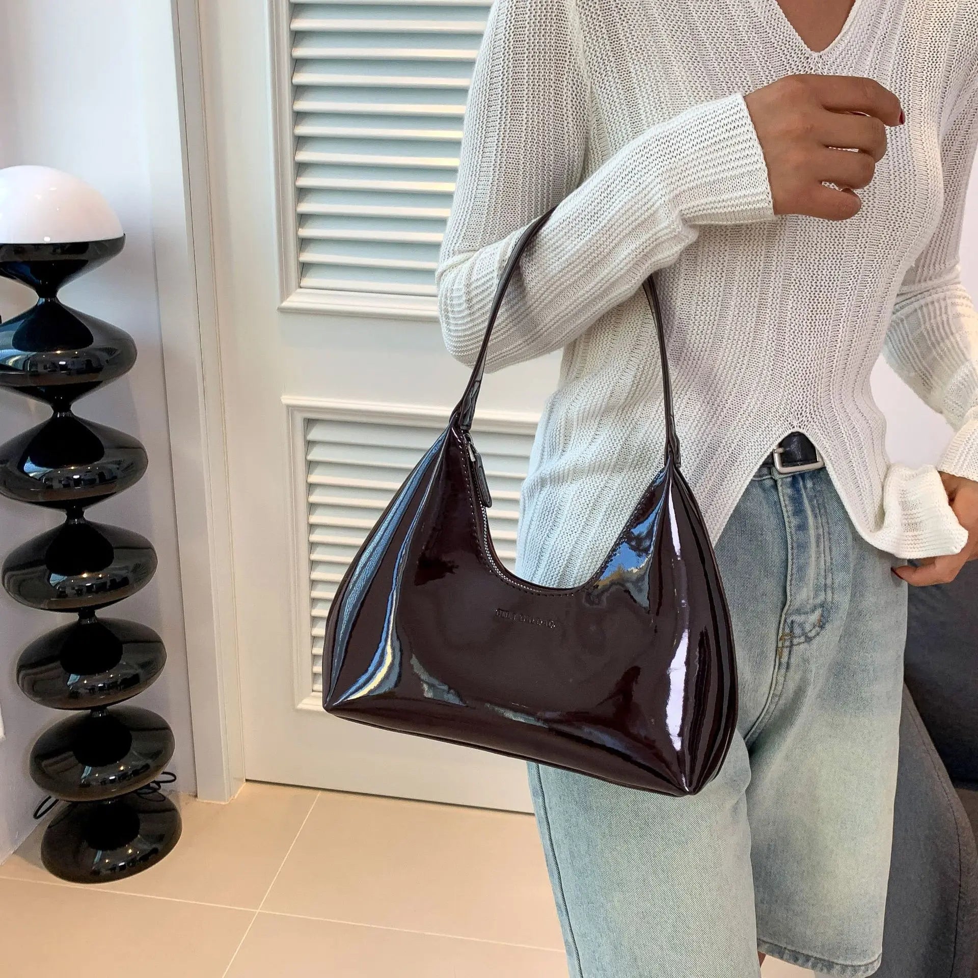 Borsa a spalla in pelle lucida marrone scuro, indossata con maglione bianco e jeans chiari. Design elegante, moda donna, accessorio di tendenza.