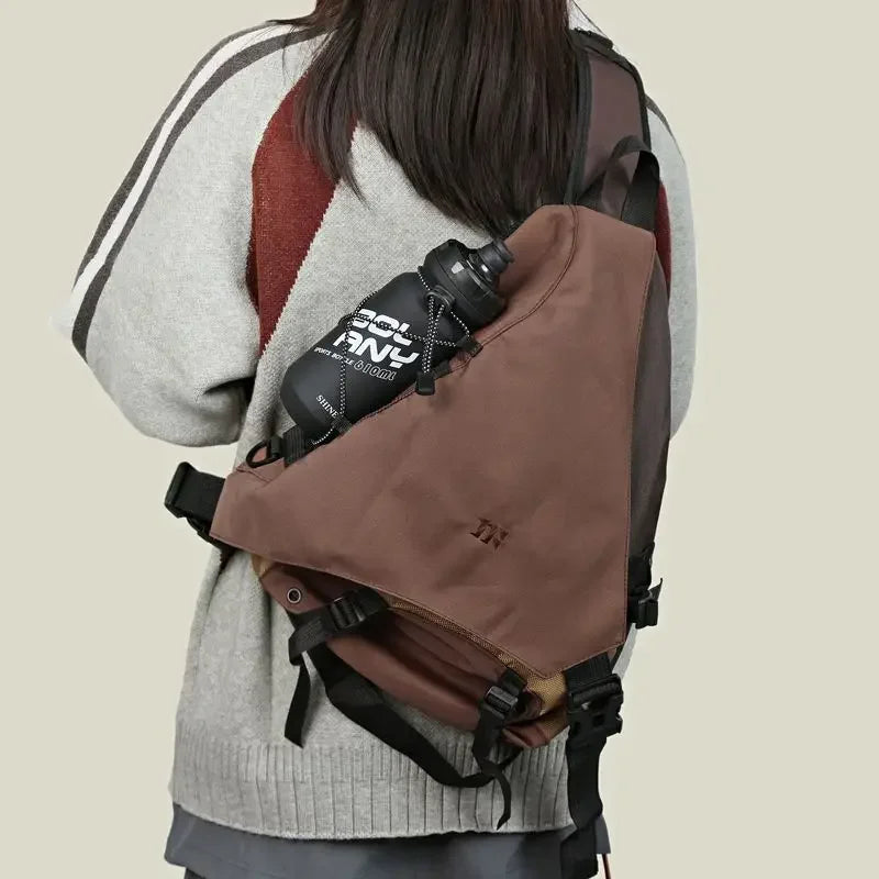Zaino a tracolla marrone con tasca per borraccia, indossato da una persona. Design moderno, ideale per escursioni e attività all'aperto.
