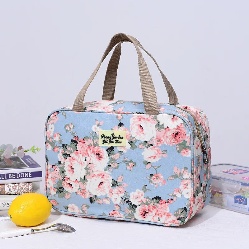 Borsa termica floreale blu con manici beige, ideale per picnic e viaggi. Design elegante con rose rosa, perfetta per conservare cibi freschi.