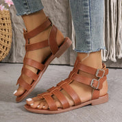Sandali gladiatore in pelle marrone da donna, con fibbie doppie, indossati con jeans. Calzature estive eleganti e comode per un look casual.