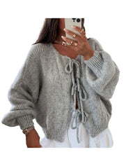Donna con cardigan grigio in maglia morbida, maniche lunghe, dettagli a fiocco, abbinato a gonna bianca. Stile casual chic, moda autunnale.