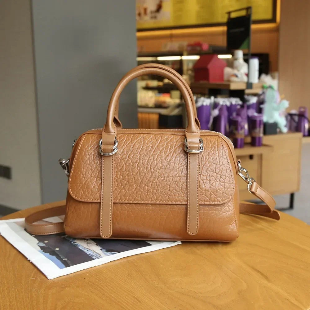 Borsa a mano in pelle marrone su tavolo di legno, design elegante con tracolla regolabile. Accessorio moda donna, stile casual chic.