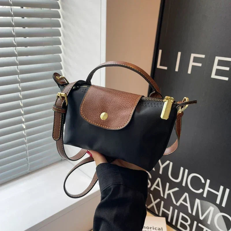 Borsa a tracolla nera e marrone con patta, chiusura a zip dorata, manico superiore e cinturino regolabile, su sfondo moderno.