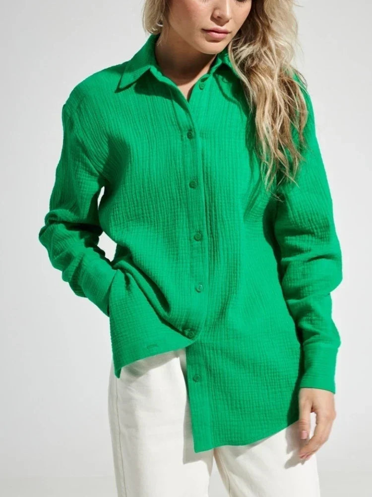Camicia verde a maniche lunghe in tessuto strutturato, indossata da una donna con pantaloni bianchi. Moda donna, abbigliamento casual elegante.