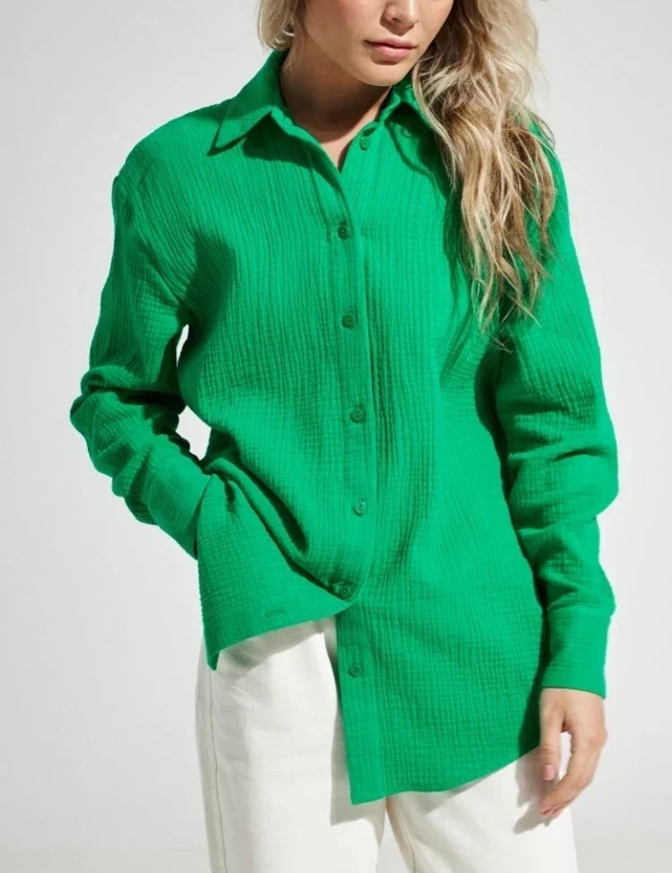 Camicia verde a maniche lunghe in tessuto strutturato, indossata da una donna con pantaloni bianchi. Moda donna, abbigliamento casual elegante.
