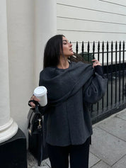 Donna con maglione grigio oversize, sciarpa abbinata, borsa nera e caffè da asporto. Moda autunnale elegante, look urbano casual.