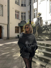 Donna elegante con occhiali da sole, mantella grigia e guanti neri, posa su una scalinata storica in città europea. Moda autunnale urbana.