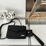 Borsa a tracolla nera elegante su tavolo bianco, accanto a calendario e poster di design. Accessorio moda donna, stile minimalista e moderno.