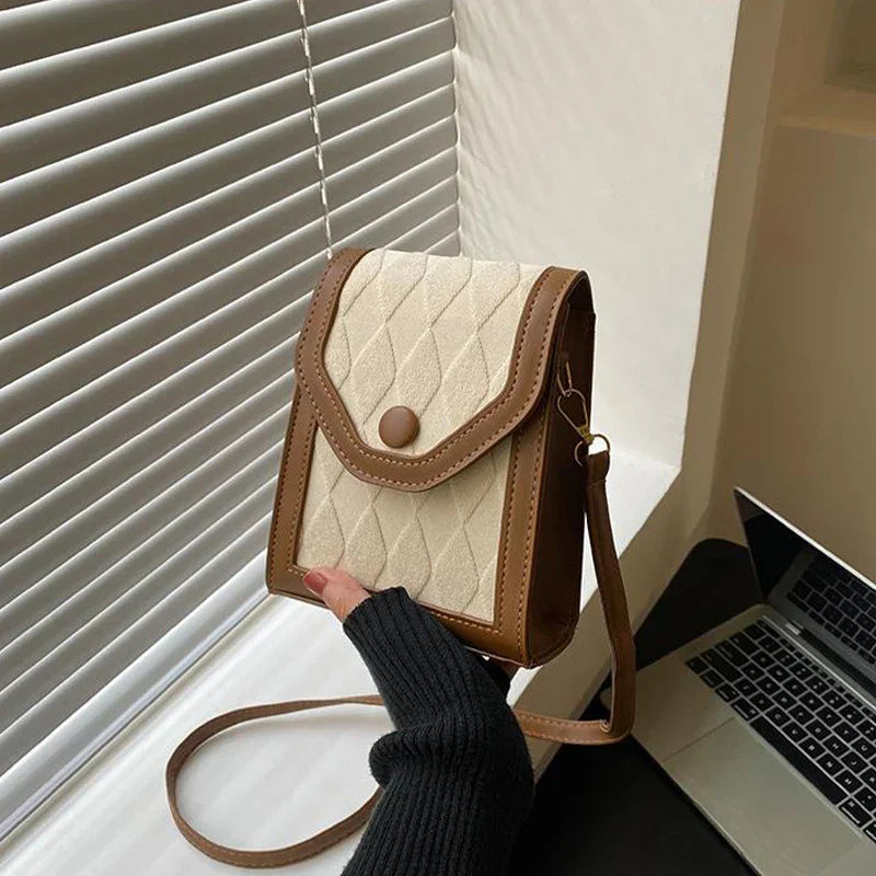 Borsa a tracolla in pelle marrone e tessuto beige, design trapuntato, chiusura a bottone, accanto a laptop su scrivania. Accessorio moda elegante.