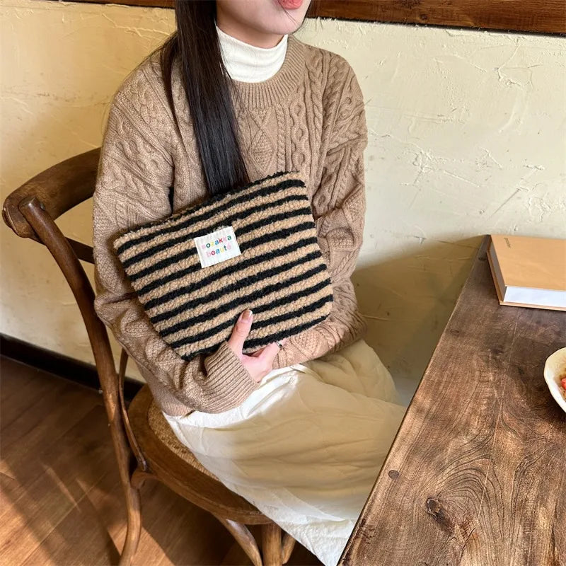 Donna seduta con maglione beige e borsa a righe nere e beige su sedia di legno. Moda autunnale, accessori invernali, stile casual chic.