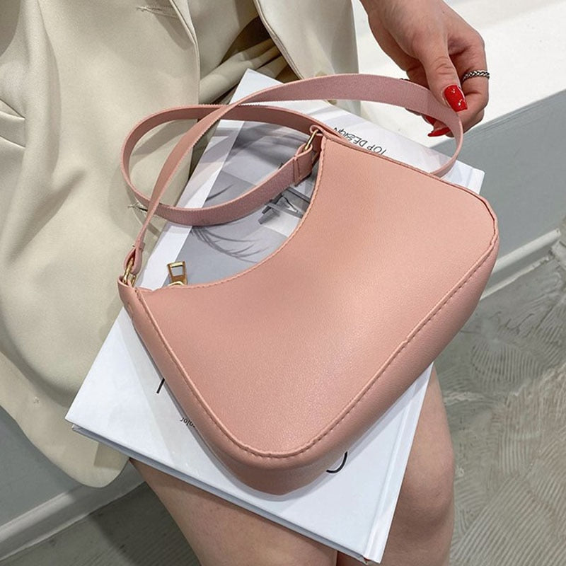 Borsa a tracolla rosa in pelle sintetica, design minimalista, chiusura a zip, indossata da una donna con smalto rosso. Accessorio moda elegante.