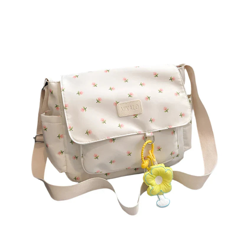 Borsa a tracolla bianca con stampa floreale, chiusura a patta, ciondolo a forma di fiore giallo, ideale per moda casual e accessori donna.