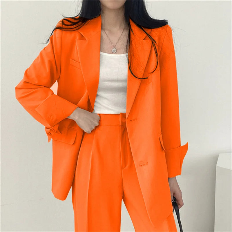 Donna in abito arancione elegante, giacca e pantaloni coordinati, indossa top bianco. Moda femminile, abbigliamento formale, tendenza colore vivace.