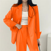 Donna in abito arancione elegante, giacca e pantaloni coordinati, indossa top bianco. Moda femminile, abbigliamento formale, tendenza colore vivace.