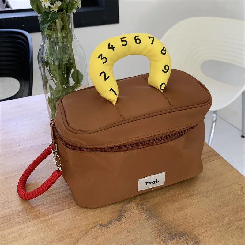 Borsa termica marrone con manico giallo numerato, design moderno, su tavolo in legno. Ideale per picnic e pranzi fuori casa.