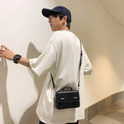 Giovane uomo con cappellino nero, t-shirt bianca oversize e borsa a tracolla nera. Moda casual uomo, accessori streetwear.