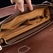 Interno di una borsa in pelle marrone con cerniera aperta, tasche multiple e cuciture a vista. Design elegante e funzionale per uomo o donna.