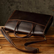 Elegante borsa ventiquattrore in pelle marrone scuro con tracolla regolabile, ideale per lavoro e ufficio. Design classico e raffinato.