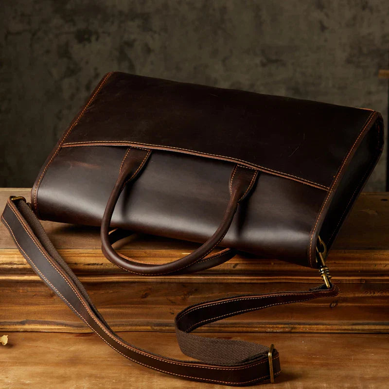 Elegante borsa ventiquattrore in pelle marrone scuro con tracolla regolabile, ideale per lavoro e ufficio. Design classico e raffinato.