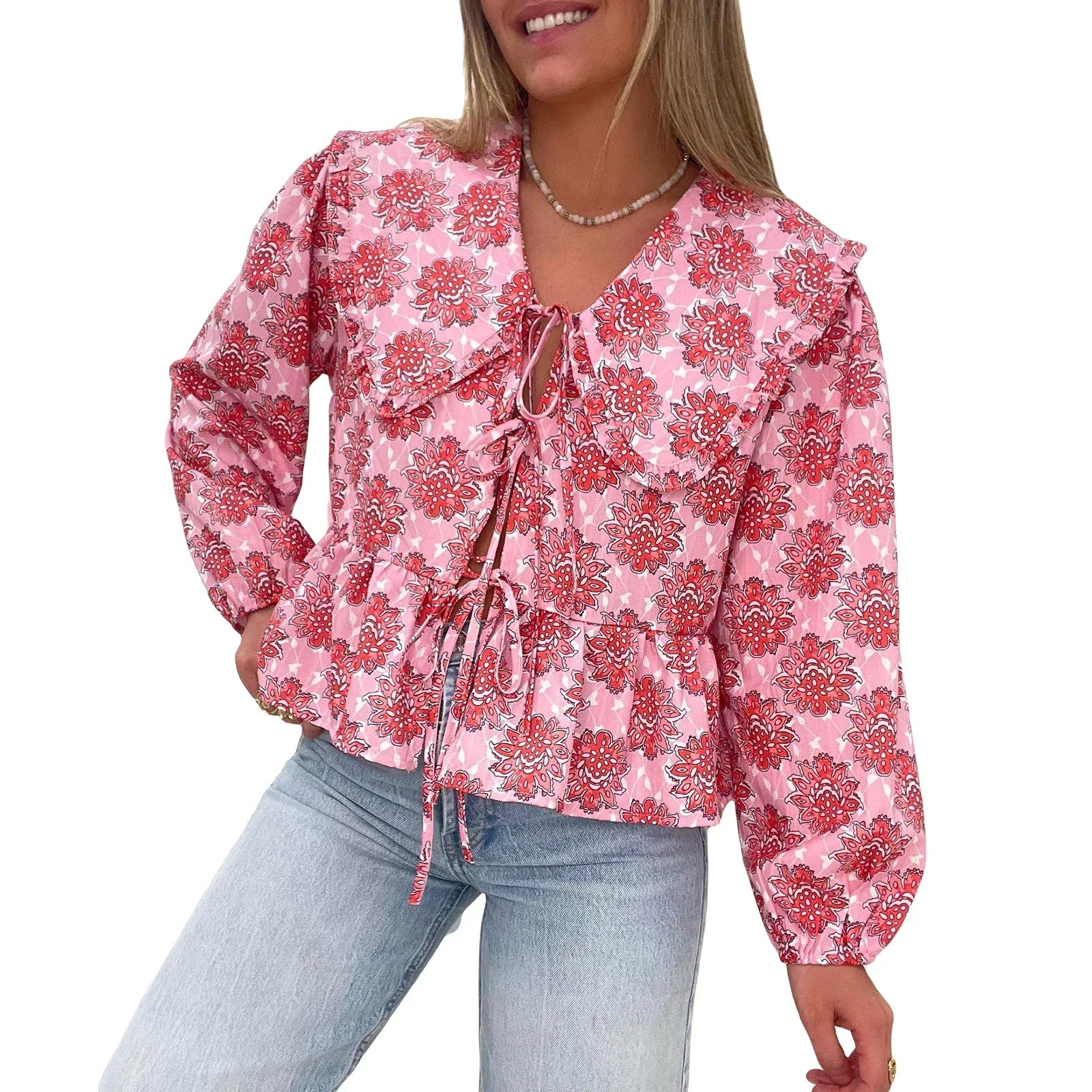 Blusa donna rosa con stampa floreale, maniche lunghe, scollo a V e laccetti, abbinata a jeans chiari. Moda femminile casual elegante.