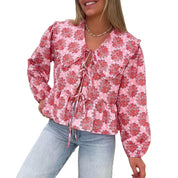 Blusa donna rosa con stampa floreale, maniche lunghe, scollo a V e laccetti, abbinata a jeans chiari. Moda femminile casual elegante.