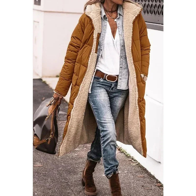 Cappotto lungo imbottito marrone donna, interno in pelliccia sintetica, abbinato a jeans e stivali marroni. Look casual autunnale.