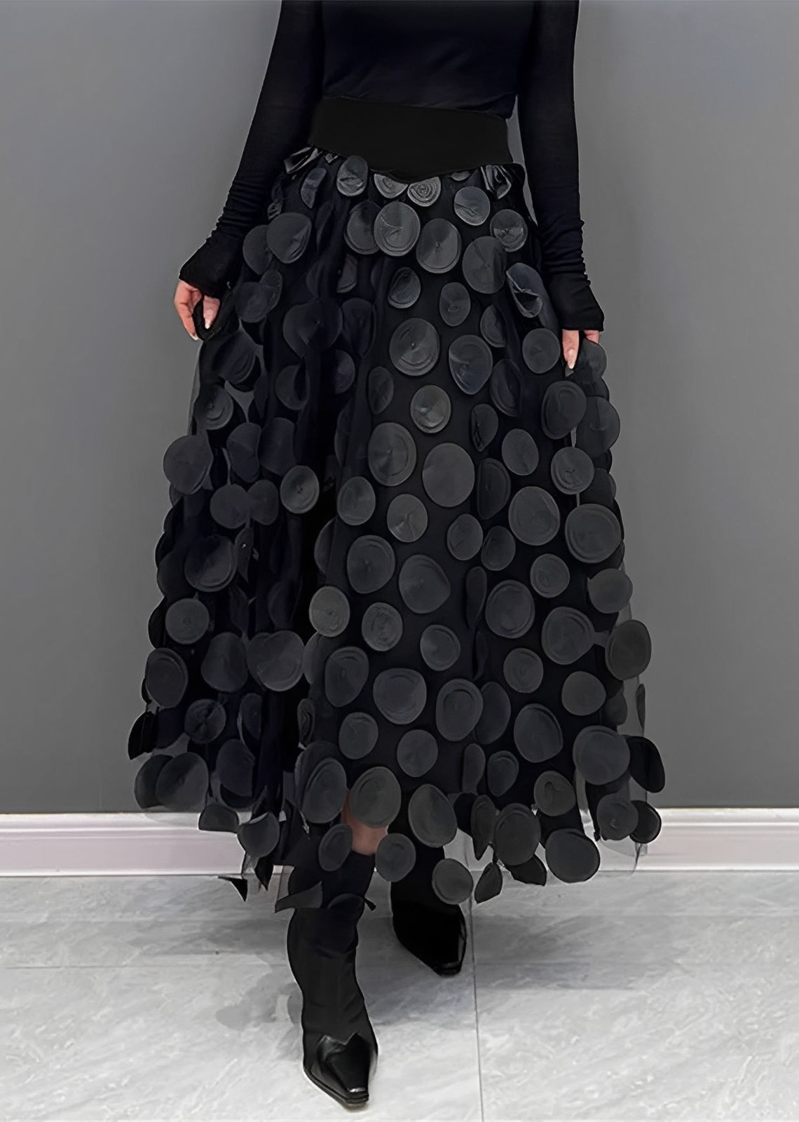 Gonna lunga nera con cerchi decorativi, indossata con top nero a maniche lunghe e stivali a punta. Moda elegante, abbigliamento femminile chic.