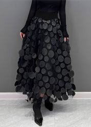 Gonna lunga nera con cerchi decorativi, indossata con top nero a maniche lunghe e stivali a punta. Moda elegante, abbigliamento femminile chic.