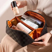 Borsa da trucco a scacchi nera con interno arancione, contenente flaconi di cosmetici e fondotinta. Organizzatore da viaggio elegante e capiente.