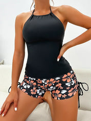 Donna in costume da bagno nero con top halter e pantaloncini floreali. Moda mare donna, abbigliamento estivo, stile casual elegante.