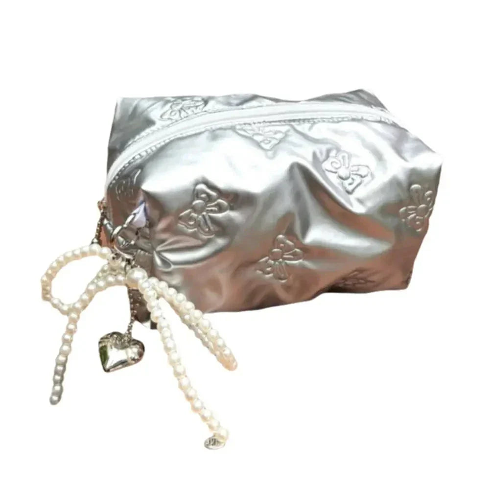 Astuccio cosmetico argento con cerniera, decorato con motivi floreali e pendente a cuore con perline. Elegante e pratico per trucco e accessori.