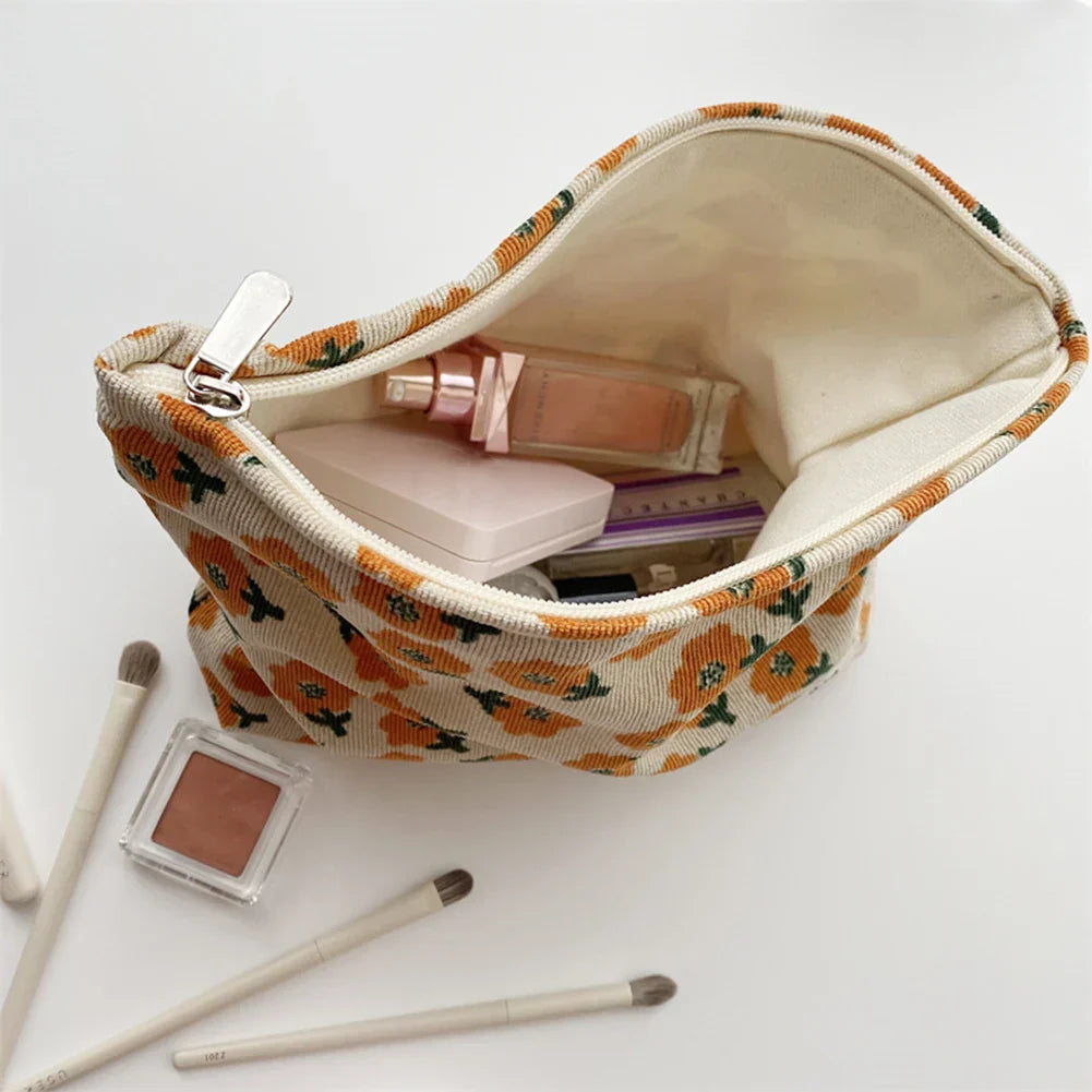 Astuccio cosmetico floreale aperto con trucchi: fondotinta, cipria, pennelli. Design floreale arancione, ideale per organizzare il make-up.