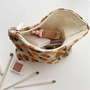 Astuccio cosmetico floreale aperto con trucchi: fondotinta, cipria, pennelli. Design floreale arancione, ideale per organizzare il make-up.