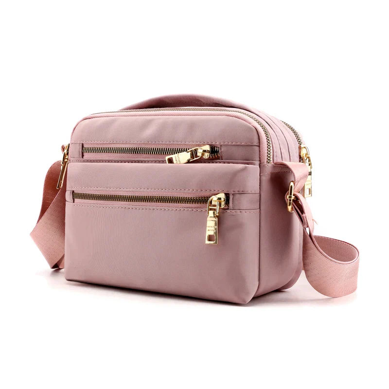 Borsa a tracolla rosa in nylon con cerniere dorate, tasche multiple e tracolla regolabile. Design elegante e pratico per uso quotidiano.