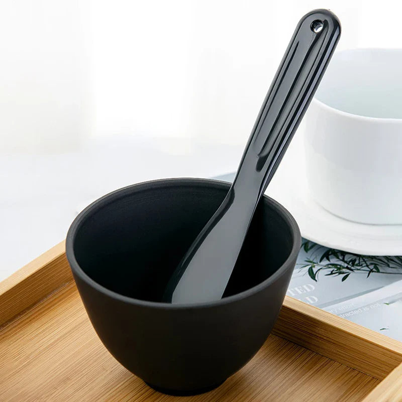 Ciotola nera in ceramica con cucchiaio su vassoio di legno, design moderno, ideale per cucina minimalista. Accessori tavola eleganti e funzionali.