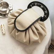 Borsa a mano beige con manico nero decorato, design elegante e moderno, su tavolo bianco. Accessorio moda femminile, stile unico e chic.