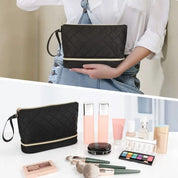 Borsa cosmetica nera trapuntata con cerniera, tenuta in mano. Include pennelli trucco, palette ombretti, fondotinta e rossetti. Accessori bellezza.