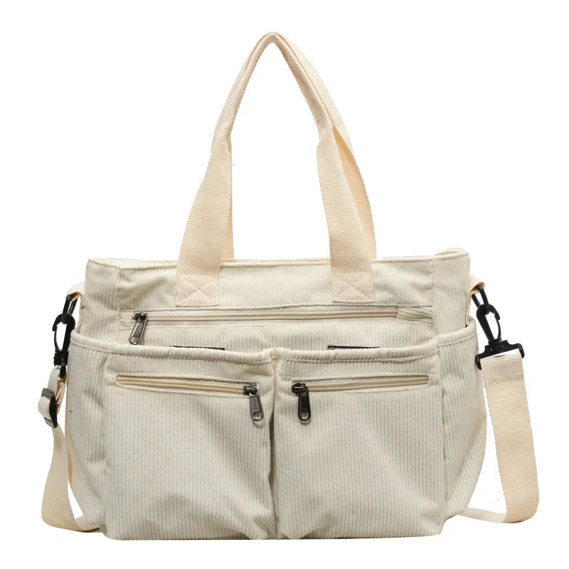 Borsa a tracolla in tessuto beige con tasche multiple e cerniere, manici robusti e tracolla regolabile. Design pratico e versatile per ogni occasione.
