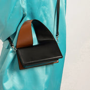 Borsa a tracolla in pelle nera e marrone su sfondo azzurro. Design moderno e minimalista, ideale per moda donna. Accessorio elegante e versatile.