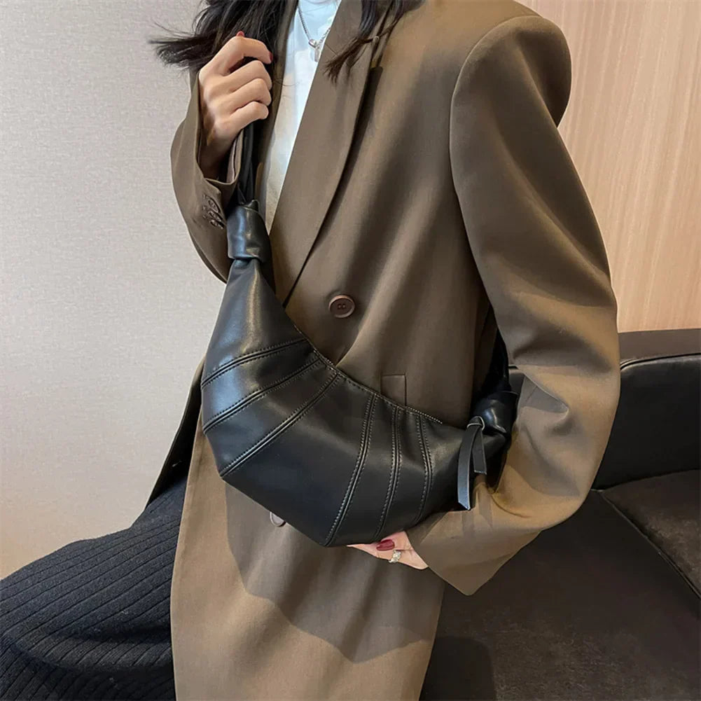 Donna con cappotto marrone indossa borsa a tracolla nera in pelle, design moderno, moda autunno inverno, accessorio elegante per outfit casual.